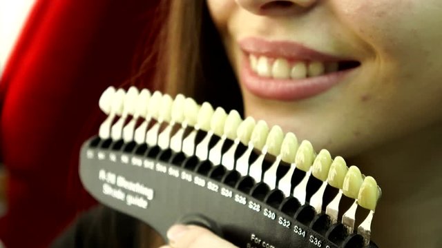 Close-up. Patient and tooth color chart. Young woman smiling. Effective teeth whitening.