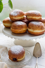 Polish donuts with plum jam on white plateau, plate. Windowsill, white concrete table.