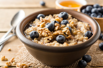 Oatmeal porridge with blueberries, walnuts and honey in ceramic bowl on wooden background.