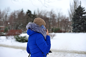 Fototapeta na wymiar Girl in a blue jacket talking on the phone in the street in the winter