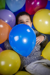 Fototapeta na wymiar Fun, Brunette boy playing with a lot of colorful balloons, smiles and joy at birthday party