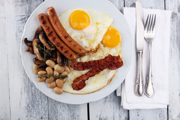 Traditional full English breakfast with fried eggs, sausages, beans, mushroomsand bacon on wooden background