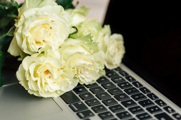 Bouquet of white roses lying on laptop. Top view