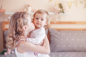 Two cute adorable white Caucasian girsl sisters kissing. Children sitting together on bed in bedroom playing. Lifestyle real true emotions, sibling love