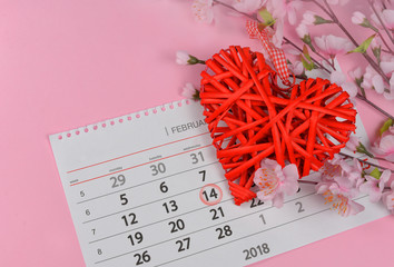 beautiful wicker red heart with pink flowers on a pink background for a valentines day holiday with a calendar on February 14