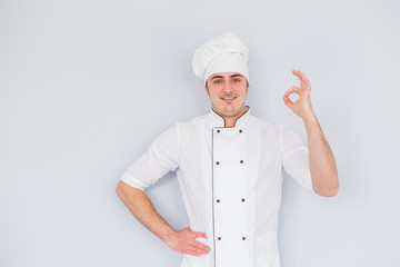 Young chef cook shows ok on a white background