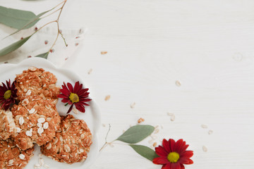 Glutenfree, homemade oatmeal cookies on a plate on white wooden table with eucalyptus and flowers