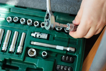 Hand with socket wrench with the socket wrench kit in a background.
