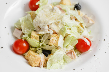 Chicken caesar salad with lettuce leaves in white bowl on wooden table