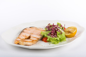 fried salmon steak with salad and lemon on a white plate isolate