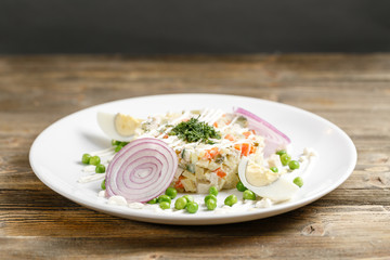 Olivier salad with trout in a white plate. Traditional Russian dish. Wooden background