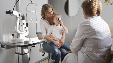 Little girl with mommy in ophthalmology - optometrist checking little child's vision
