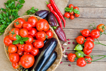 Tomatoes, eggplants in basket and other vegetables on sacking and wooden background