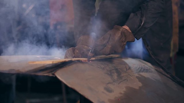 Male worker in protective workwear is cutting pieces off metal construction with oxy acetylene cutting torch