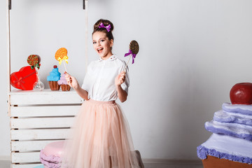 Beautiful teenage model girl in pink tutu or tulle skirts with colorful pink and yellow lollipops in studio on white background  with artifitial big macaroons, fancy cakes and sweets