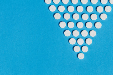 Medication white round tablets arranged in form of inverted triangle isolated on blue background. Pills geometric pyramid shape. Concept of health, treatment, choice, healthy lifestyle. Copy space.