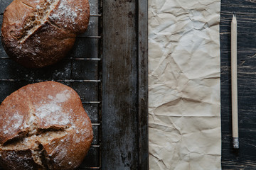 Homemade rustic bread on a baking tray over old, black wooden background with paper and pencil