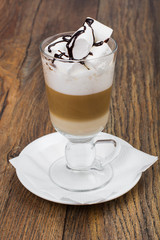 Tall glass with latte and marshmallow on wooden table