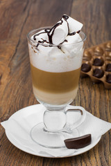 Tall glass with latte and marshmallow on wooden table