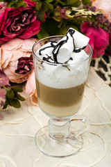 Tall glass with latte and marshmallow on wooden table