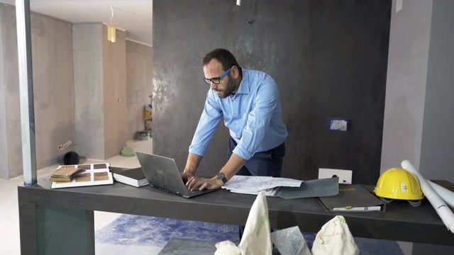 Young man working with laptop by table at new home
