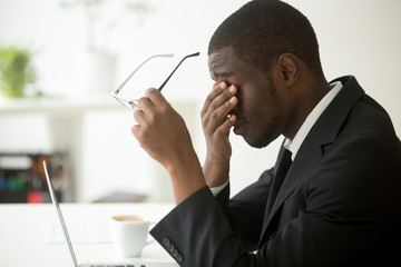 Tired of computer african businessman taking off glasses feels eye strain fatigue after long office...