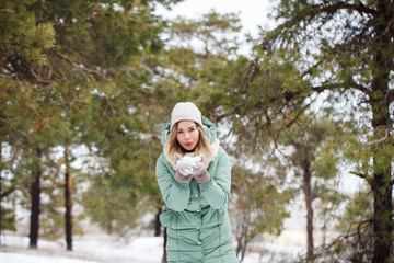 Obraz premium Attractive beautiful girl holds snow in hands and smiles. Portrait of a slender cute girl on a winter background, looking at the camera and smiling. Space for text