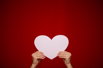 Hands hold white paper heart on red background. Valentines day composition