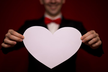 Stylish man in suit hold white paper heart, with red background, focus on heart. Valentines day composition