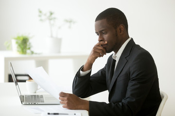 Serious african-american businessman employer thinking of business offer reading mail cover letter...