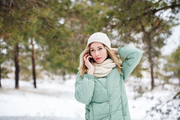 Beautiful girl talking on cell phone looking at camera and smiling. Portrait of attractive girl outdoors in winter, which communicates on smartphone. Space for text.