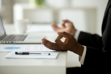 African american calm businessman relaxing meditating in office, peaceful ceo in suit practicing...