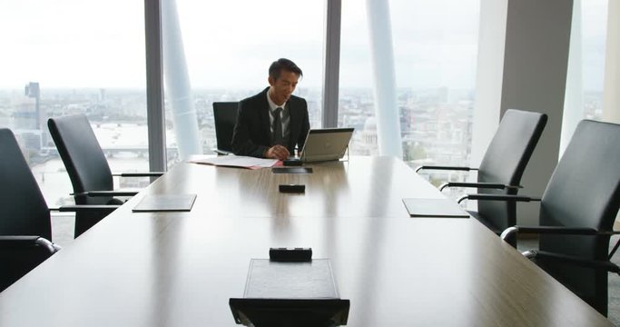 4K Successful businessman working alone in office boardroom gets up to look at view of the city