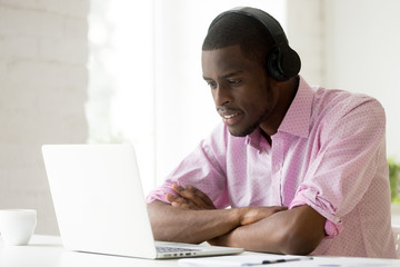 African american man wearing headphones using laptop looking at computer screen, smiling young black businessman learning studying online, watching video or making call with pc internet application