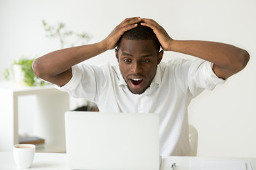 Amazed excited african-american man surprised by unexpected good news win result online, astonished black businessman looking at laptop screen with wow face wonders unbelievable fantastic email offer