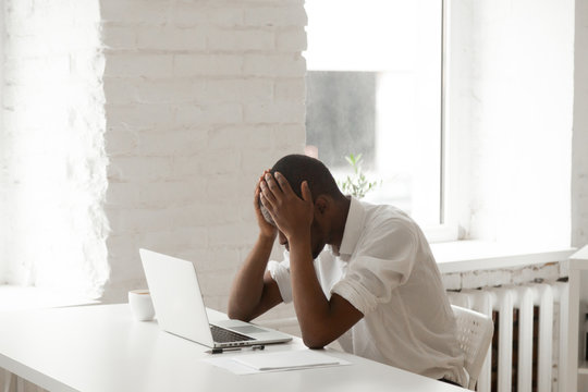 Stressed Black Businessman In Panic After Business Failure Sitting At Office Work Desk In Front Of Laptop, Frustrated Desperate Bankrupt African American Man Feeling Distraught Depressed About Debt