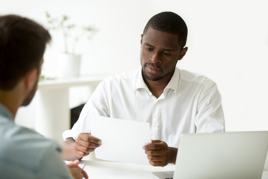 Serious african businessman reading document at meeting, black entrepreneur considering contract, company ceo analyzing report, hr manager or employer holding applicants cv resume at job interview