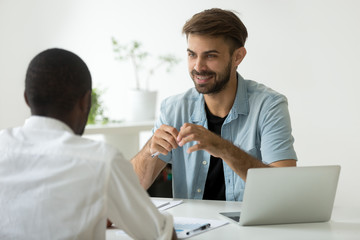 Smiling friendly caucasian businessman discussing new project with black colleague at office desk, diverse coworkers talking share ideas at work, company manager teaching african intern at workplace
