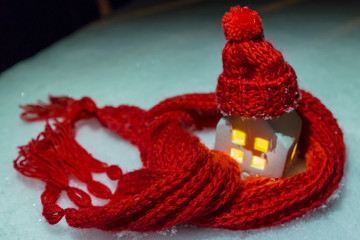 a toy house in the snow in a scarf and hat. the concept of saving and saving heat and resources.