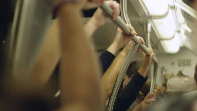 Slow motion of people's hands holding onto railings inside a moving train

