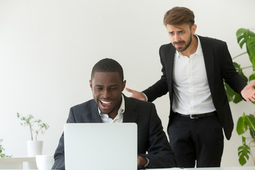 Angry confused white boss catching african american employee entertaining online instead of work,...