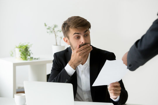 Surprised confused caucasian employee receiving dismissal notice, letter or document with unexpected news from african boss, worried shocked office worker getting fired in written message at work