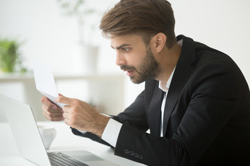 Amazed businessman in suit feeling shocked by reading mail, surprised entrepreneur stunned by...