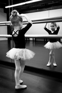 Cute little ballerina dreaming of becoming a dancer. Young girl practicing her ballerina pose looking in the mirror.