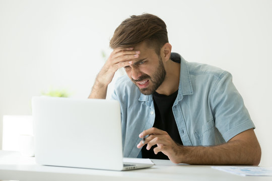 Confused young man frustrated by online problem looking at laptop screen, worker troubled doing hard job on computer making notes, student feels stressed about difficult learning failing test or exam