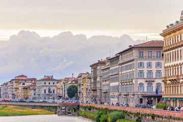 Fototapeta na wymiar Daylight cloudy day view to Arno river with sunset reflections and cars riding on bridge