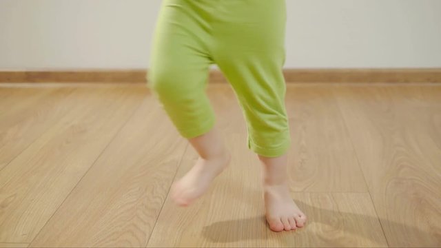 Closeup of the legs of a young child dancing and stomping on a wooden floor in a room