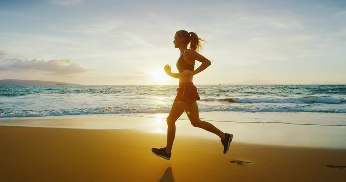 Athletic young woman running on the beach at sunset
