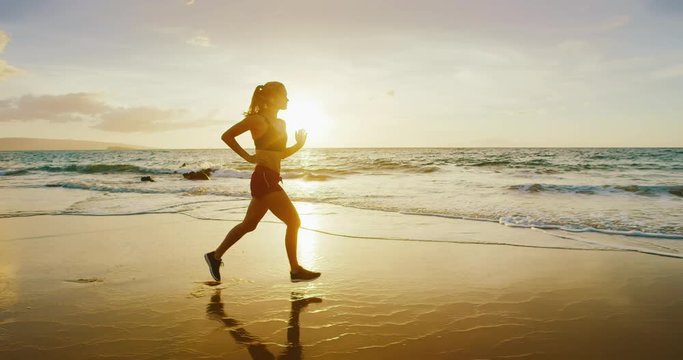 Athletic young woman running on the beach at sunset