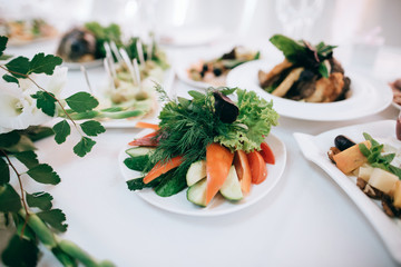 Wedding reception white table arrangement, floral centerpiece decoration, food. Catering service.